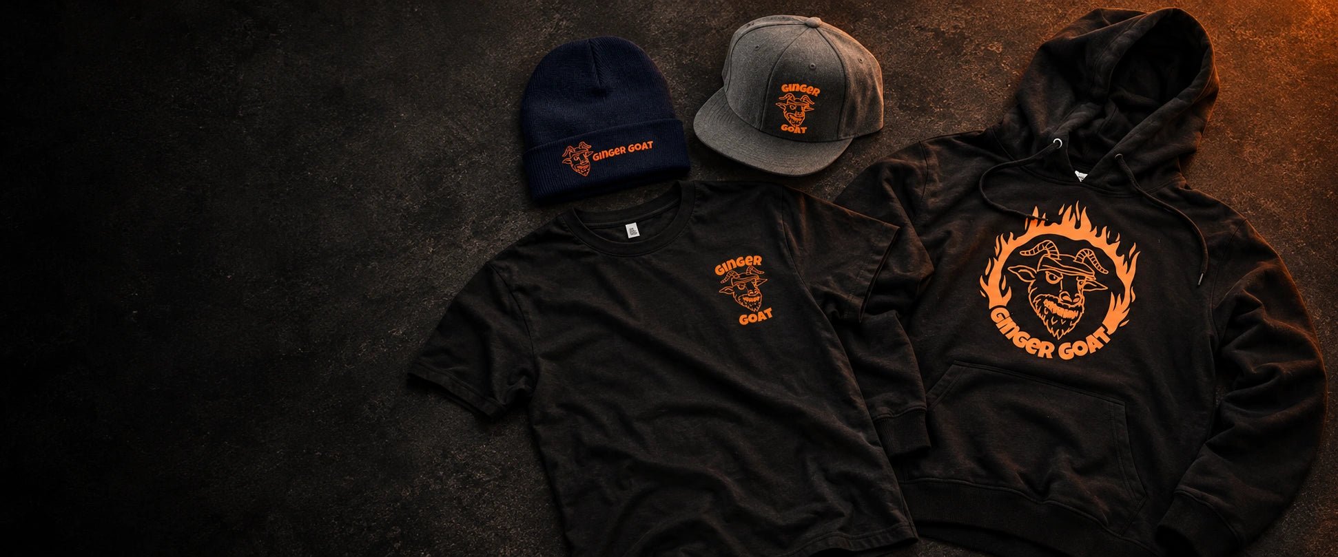 Ginger Goat black Ring of Fire hoodie, logo T-shirt, grey snapback and navy toque arranged together on a charcoal surface